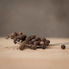 Whole Black Pepper Corns on Metal Spoon on Wooden Chopping Board.