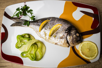Dorada fish cooked in the oven with lemon, pimento and green onion served on a tray on a wooden table