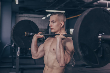 Fototapeta na wymiar Muscular shirtless man working out at the gym, lifting barbell. Handsome sexy ripped fitness man exercising at sport studio, copy space. Motivation, athletics, crossfit concept