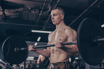 Fototapeta na wymiar Shirtless muscular male crossfit athlete lifting barbell at the gym, copy space. Handsome young athletic man with sexy ripped torso working out with barbell. Sport, motivation, fitness concept