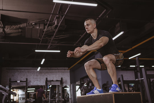 Low angle full length shot of a male crossfit athlete box jumping, working out at the gym. Attractive sportsman exercising at sports studio, jumping on a box. Endurance, active lifestyle concept, copy