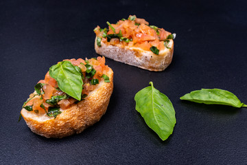 Tasty savory tomato Italian appetizers, or bruschetta, on slices of toasted baguette garnished with basil and avocado