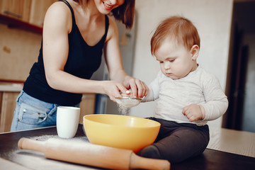 A young and beautiful mom is preparing food at home in the kitchen, along with her little son