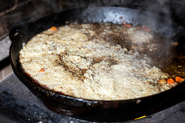 cooking Rice for pilaw or paella in iron cauldron over open fire. Smoke and steam. Tasty food preparing outdoor process background