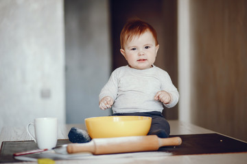 little boy sitting at home on a table in the kitchen near a plate of flour