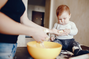 A young and beautiful mom is preparing food at home in the kitchen, along with her little son