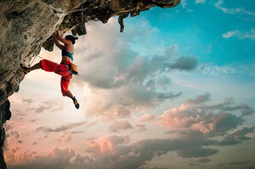 Foto op Plexiglas Atletische vrouw klimmen op overhangende klif rots met zonsopgang hemelachtergrond © Soloviova Liudmyla