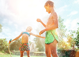 Brother and sister have fun, when play with watering hose in summer garden