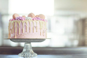Pink cake decorated with macaroons on the table.