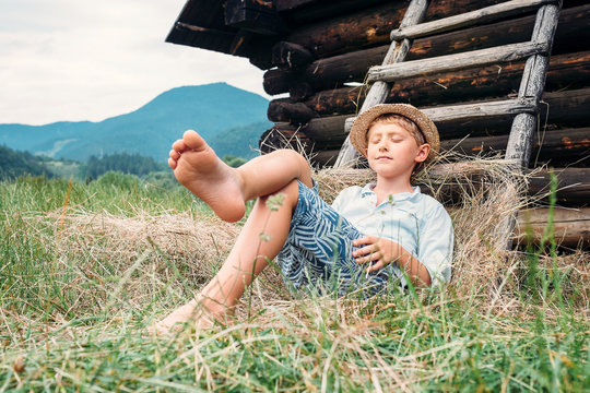 Boy in straw hat lies in hay near the barn