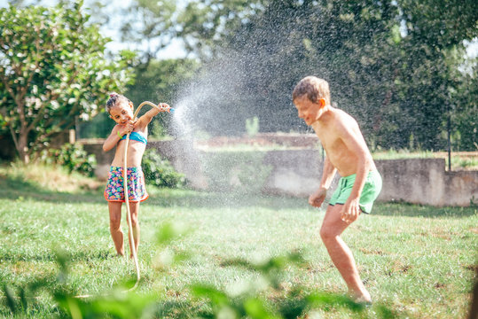 Two childs playing in garden, pours each other from the hose, makes a rain. Happy childhood concept image.