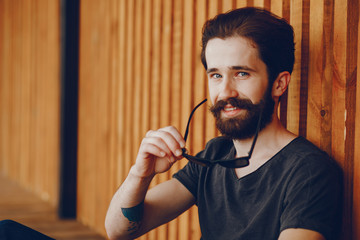 Beautiful guy with a tattoo. A man sitting near wall. The guy with a sunglasses