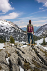 Naklejka premium Girl with purple backpack standing on mountain peak looking to beautiful view over the european Alps in Austria.