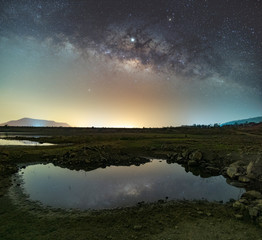 The stars in the sky reflect the light at night. The Milky Way above the mountains and the pond Mae Prachan Dam and Reservoir, Phetchaburi, Thailand