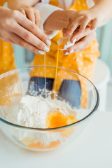 cropped view of mother and daughter smashing egg into bowl with flour