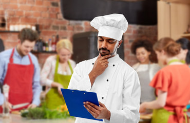 cooking class, profession and people concept - male indian chef in toque reading menu on clipboard...