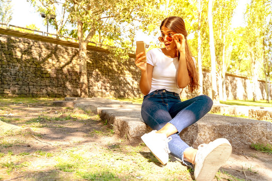 A surprised young woman sitting and using her smartphone