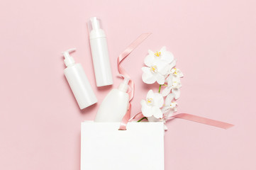 Cosmetics SPA branding mock-up. Flat lay top view White cosmetic bottle containers gift bag White Phalaenopsis orchid flowers on pink background. Natural organic beauty product concept