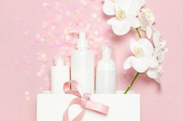 Obraz na płótnie Canvas Flat lay top view White cosmetic bottle containers festive confetti gift bag White Phalaenopsis orchid flowers on pink background. Cosmetics SPA branding mock-up Natural organic beauty product
