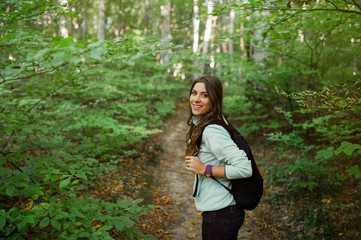 Young woman taking a walk in the forest, carrying a backpack in the forest on sunset light in the autumn season.