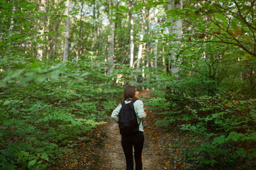 Fototapeta na wymiar Young woman taking a walk in the forest, carrying a backpack in the forest on sunset light in the autumn season.