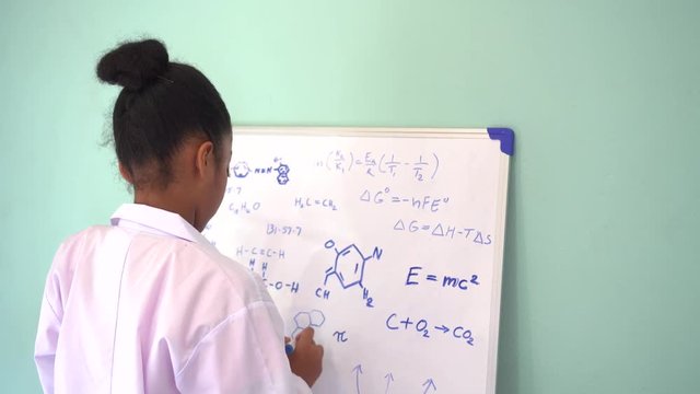 African American girl in lab coat drawing mathematic and science formulas on white board. Creativity and Education concept