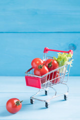 Food minimal concept, natural organic tomatoes in a toy shopping cart on a blue wooden background...