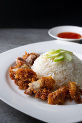 Hainanese chicken rice or rice cooked in chicken broth with fried chicken in the white dish.