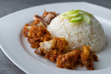 Hainanese chicken rice or rice cooked in chicken broth with fried chicken in the white dish.