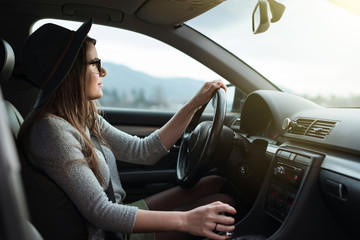 Young hipster woman with eyeglasses and hat driving the car.  - obrazy, fototapety, plakaty