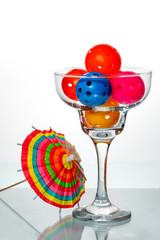 Pickleball Cocktail with umbrella colorful Pickleballs in a Margarita glass with a drink umbrella on the side and a white background