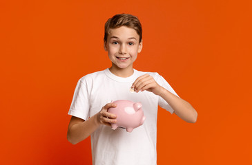 Little boy putting pocket money in piggy bank