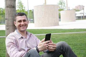 close-up. Portrait of a handsome young man talking on a smartphone and smiling while sitting on green grass in a park.