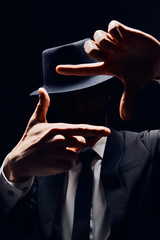 Faceless man in suit and hat looking through a finger frame