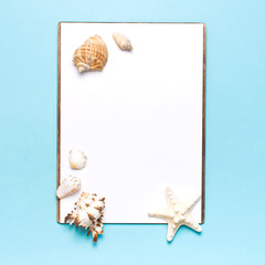 Summer concept, marine background. Seashells, starfish, white blank sheet on pastel blue background. Top view, flat lay, copy space. Sea summer vacation Mockup. Travel, marine souvenir