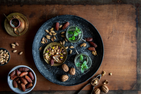 Healthy teatime oriental style with mint tea, dates, walnuts and pistachios  on black ornamental tray over wooden background