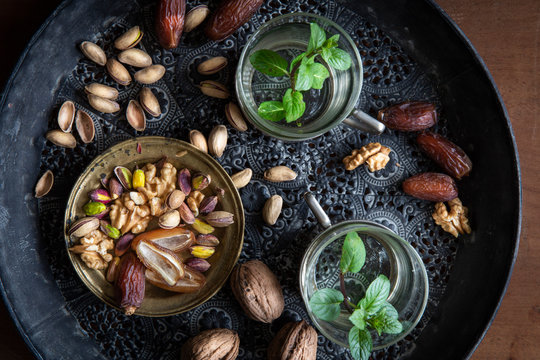 Healthy teatime oriental style with mint tea, dates, walnuts and pistachios  on black ornamental tray over wooden background