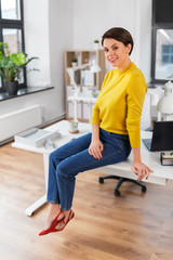 business and people concept - happy businesswoman sitting on desk at office