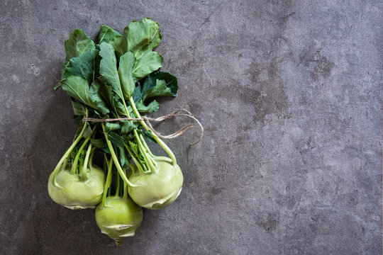 Bundle of fresh kohlrabi stems with leafs over grey concrete background