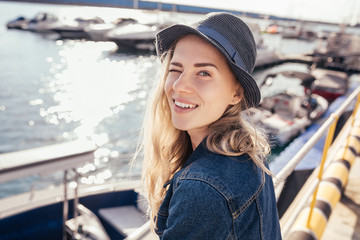 Positive young student girl posing against the backdrop of the sea pier and winking with one eye...