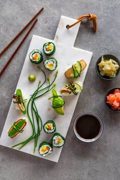 Vegan maki and nigiri sushi on white marble board over grey concrete background
