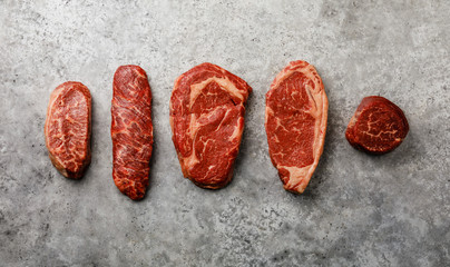 Variety of Raw Black Angus Prime meat steaks Top Blade, Denver, Rib Eye, Striploin, Tenderloin fillet Mignon on gray background