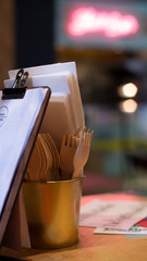A close up of a golden pot filled with white napkins and wooden recycled forks, a great and eco friendly replacement of the plastic forks. A contemporary eating establishment. 
