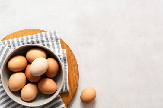 Fresh hen eggs in a bowl on a textured grey background with copyspace.