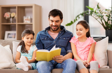 family, leisure and people concept - happy father with daughters reading book at home