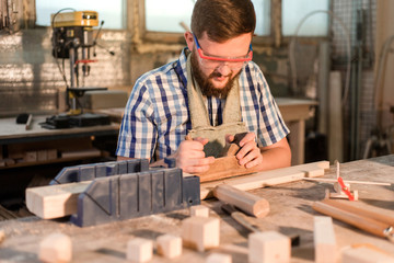 Working days of a professional carpenter in a home workshop, a craftsman at his workplace is planing a tree with a planer