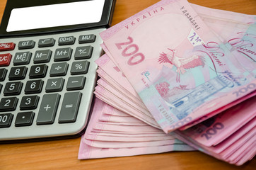 200 hryvnia and a calculator on a wooden table. Close-up.
