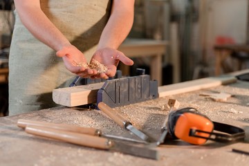 Bearded carpenter standing at the table holding sawdust in the home workshop