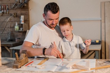 Father and son in the carpenter's shop draw a project for the production of toy wooden aircraft