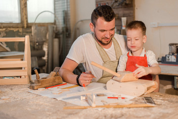 Father and son in the carpenter's shop playing with wooden toys made with their own hands. Paternal care. Teaching a child craft